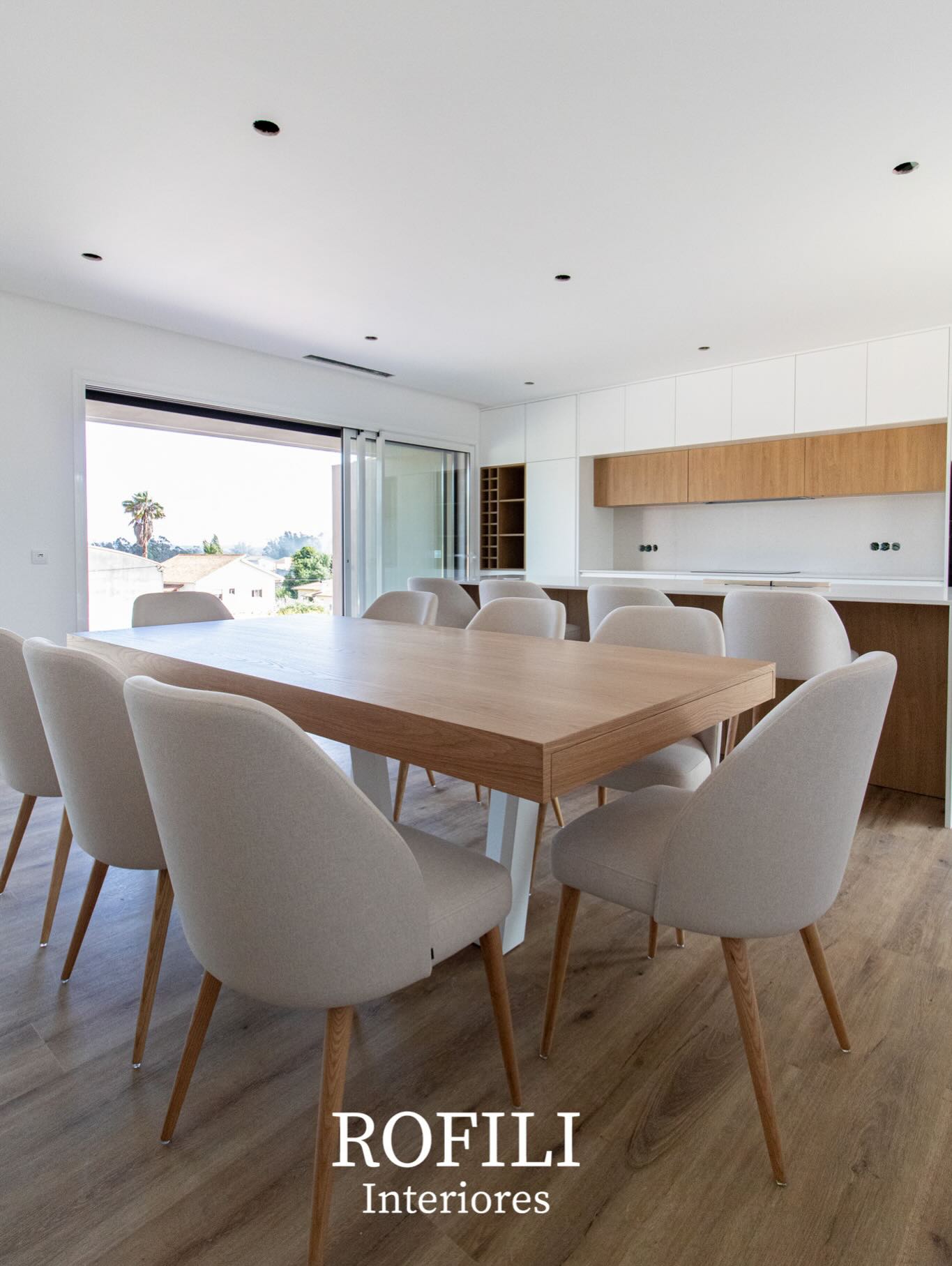 Sala de jantar com mesa em madeira, cadeiras estofadas e mobiliário fixo em composição com a cozinha aberta